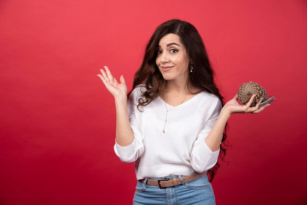 Elegant woman holding a big Christmas pinecone on red background. High quality photo