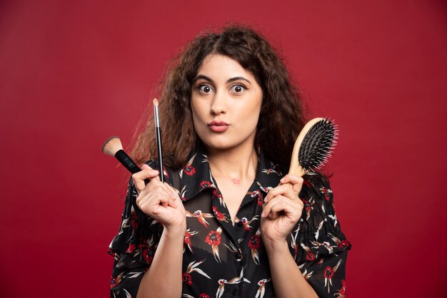 Elegant woman holding makeup brushes and comb.