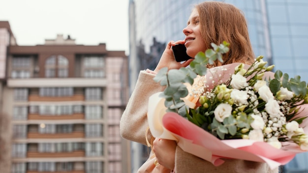 Элегантная женщина на открытом воздухе разговаривает по телефону и держит букет цветов