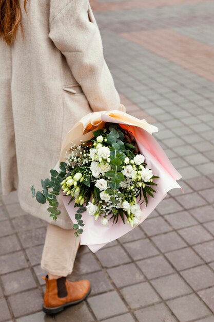 花の花束を屋外で歩いて保持するエレガントな女性