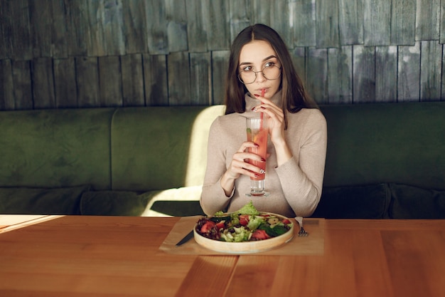 Elegant woman sitting at the table with cocktail and salad
