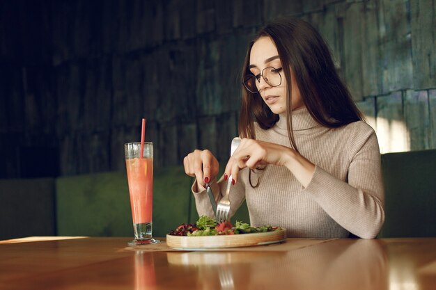 Элегантная женщина сидит за столом с коктейлем и салатом