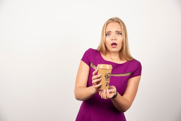 Elegant woman with cup of coffee posing with surprised expression.