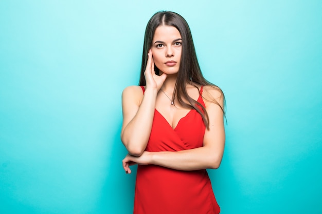 Elegant young attractive woman wearing red summer dress with hands on chin isolated over pastel blue wall.