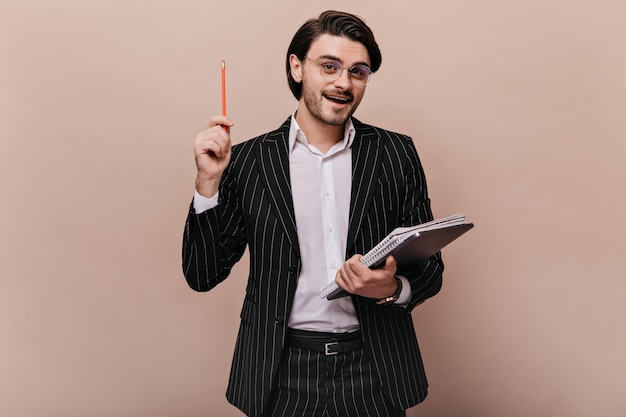 Elegant young teacher with brunette hair, in stylish light shirt, black striped suit, glasses holding writings, pen, and giving lecture