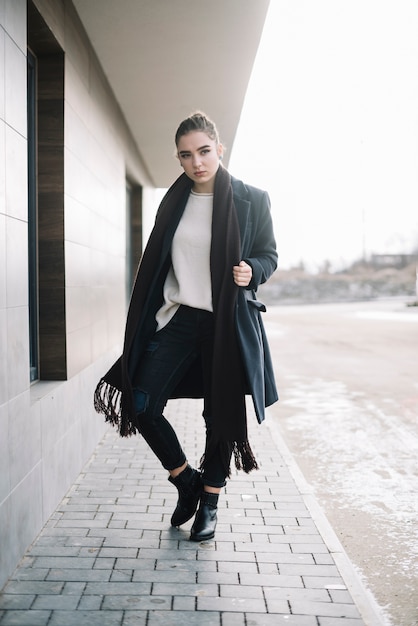 Elegant young woman in coat with scarf on street