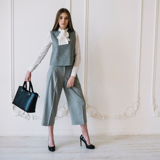 Elegant young woman in costume with handbag in room