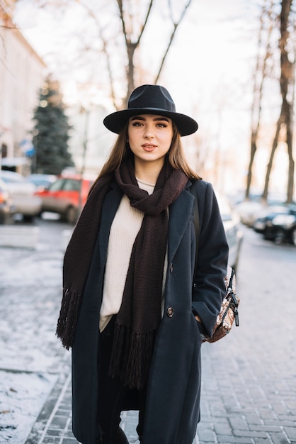 Elegant young woman in hat and coat with scarf on street