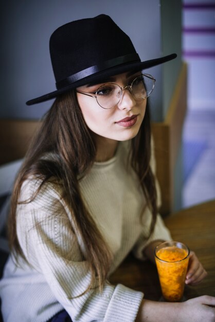 戴着帽子和眼镜的优雅的年轻女人,拿着一杯饮料