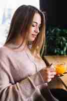 Free photo elegant young woman holding cup of drink at bar counter in cafe