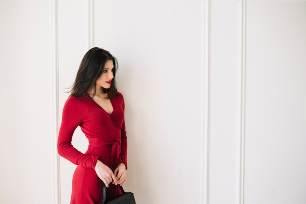 Elegante giovane donna in abito rosso con borsetta in camera