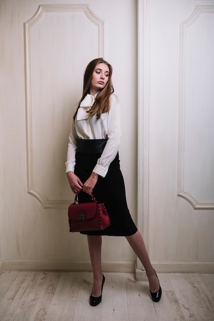 Elegant young woman in skirt and blouse with handbag in room