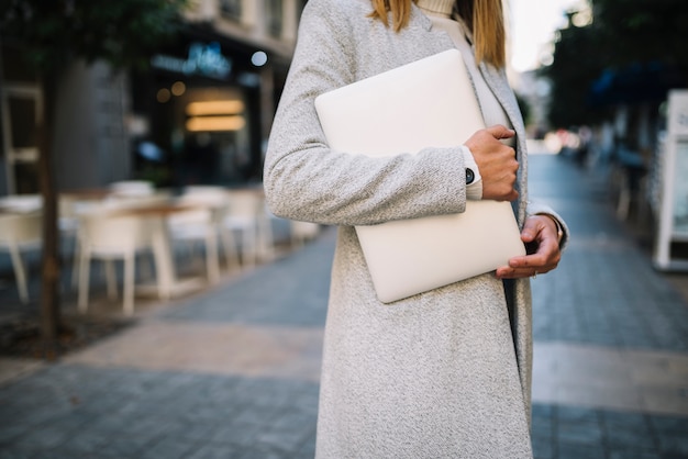 Giovane donna elegante con il computer portatile sulla via