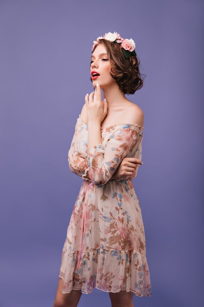 Elegant young woman with short haircut posing with flowers on her head. Indoor portrait of fashionable girl in stylish summer dress.