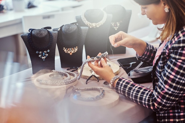 Free photo elegantly dressed woman makes handmade necklaces, working with needles and thread in jewelry workshop.