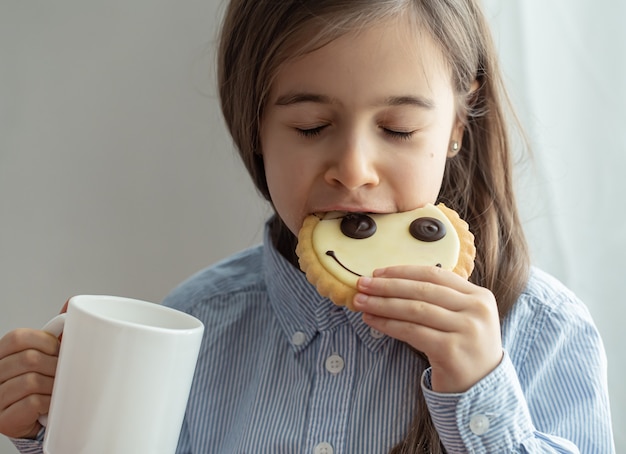 小学生の女の子がスマイリーの形でミルクと面白いクッキーで朝食を食べています