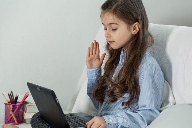 A elementary school girl studies at home using a laptop remotely during quarantine due to the coronavirus pandemic.