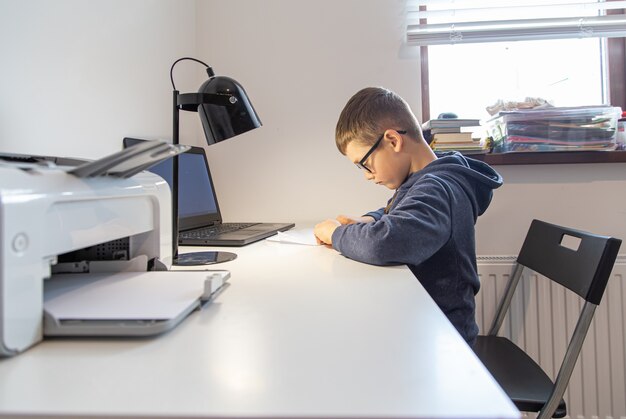 An elementary school student learns remotely at home in front of a laptop at his desk.