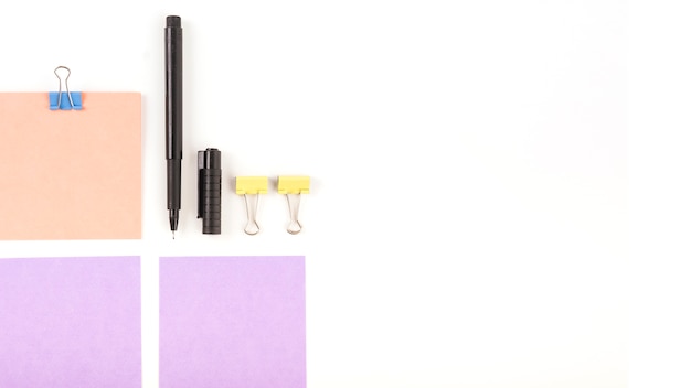 Elevated view of adhesive notes; pen and bulldog clips on white background