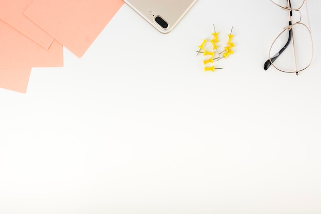 Elevated view of adhesive notes; smartphone; push pins and spectacles at the top of white background