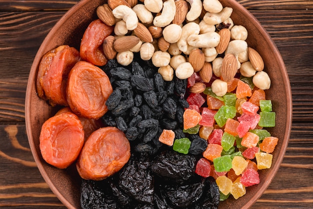 An elevated view of apricot; dried fruits; black raisin and nuts in bowl on wooden surface
