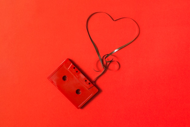 Elevated view of audio cassette with tangled heart shape tape on red background