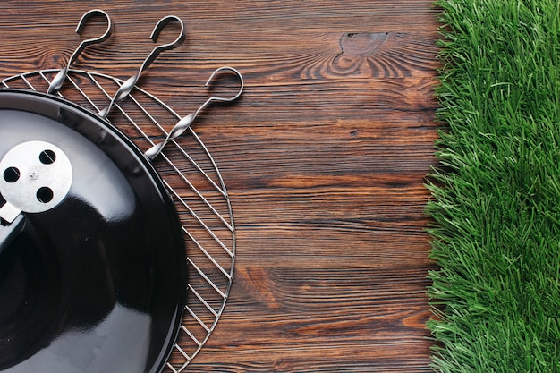 Elevated view of barbecue appliance and metallic skewer on wooden background