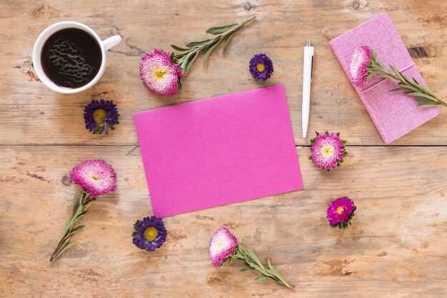 Elevated view of beautiful flowers; blank pink paper; pen; diary and black tea on wooden surface