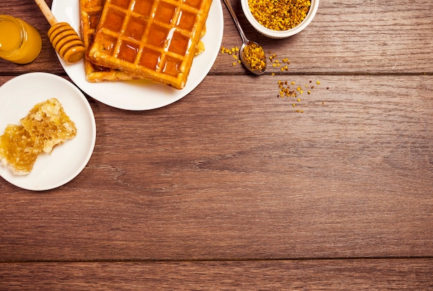 Elevated view of belgium waffle with honey and bee pollen on wooden textured