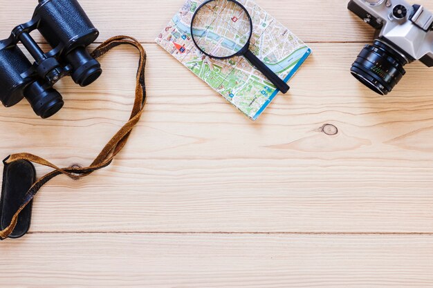 Elevated view of binoculars; magnifying glass; map and camera on wooden surface