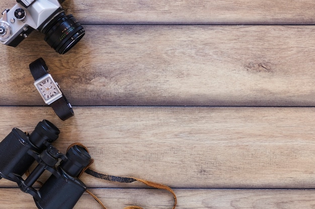 Elevated view of binoculars; wrist watch and camera on wooden backdrop