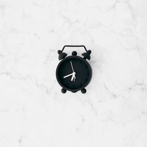 An elevated view of black alarm clock on white textured wallpaper