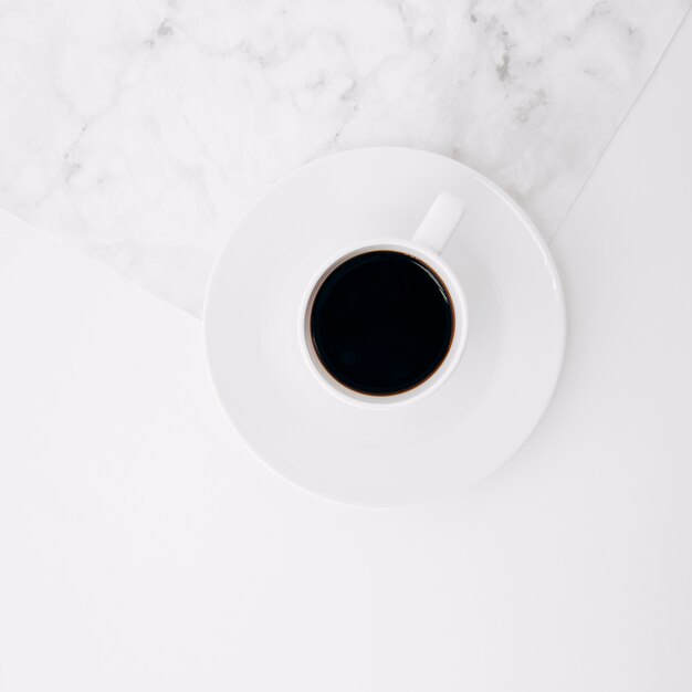 Поднятый вид черного кофейной чашки на блюдце на мраморном и белом фоне