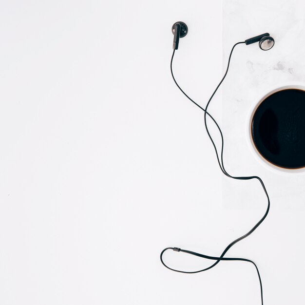 An elevated view of black earphone and coffee cup on white background
