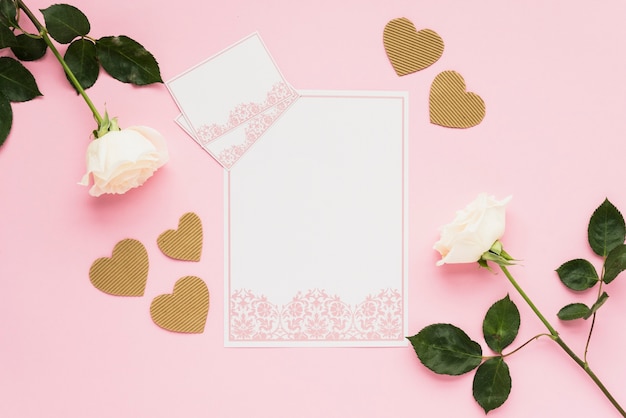 Elevated view of blank cards with golden hearts and roses on pink surface