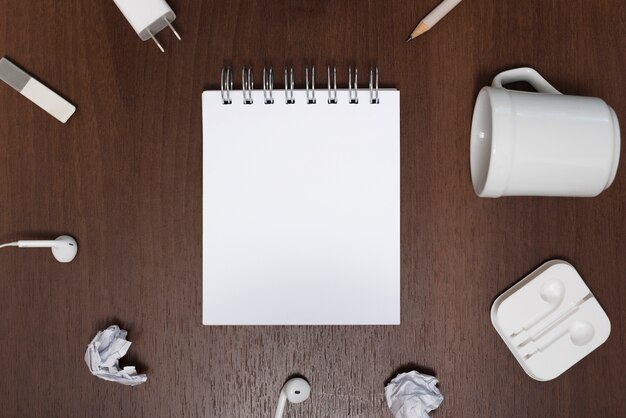 Elevated view of blank notepad surrounded by crumpled paper; empty cup on wooden background