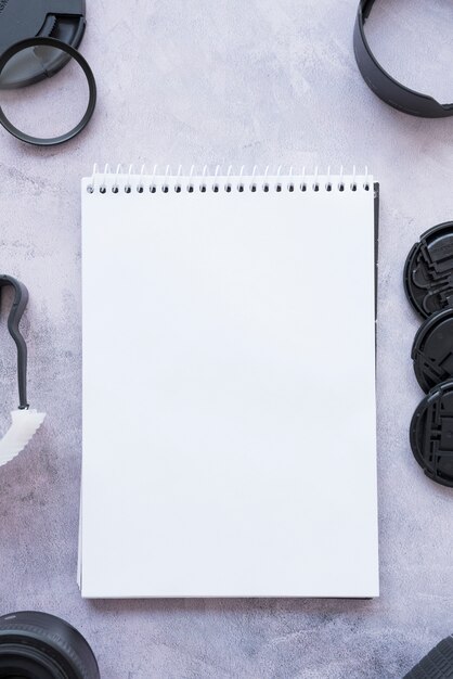 Elevated view of blank opened spiral notepad with camera accessories on concrete background