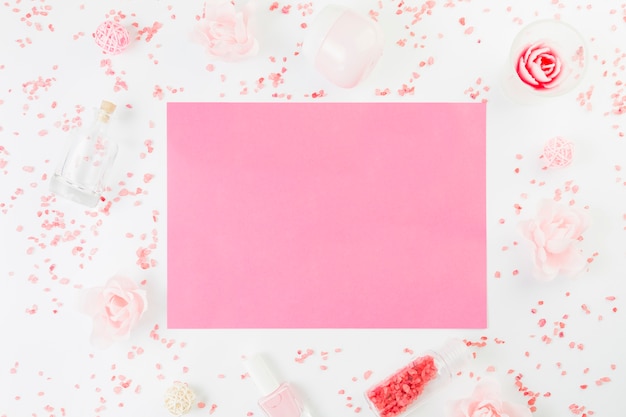 Elevated view of blank pink paper surrounded with beauty products on white surface