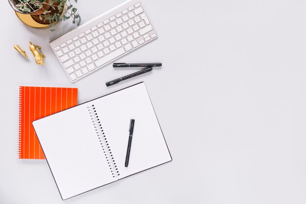 Elevated view of blank spiral diary; pen; keyboard and golden animal miniature statue on white background