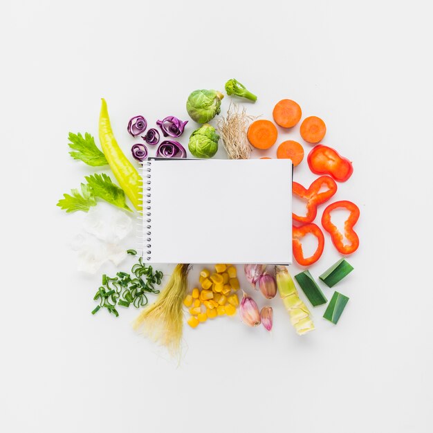 白い背景の上に新鮮な野菜の空白のスパイラルメモ帳の上昇したビュー