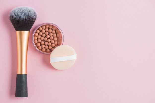 Elevated view of bronzing pearls; sponge and makeup brush on pink backdrop