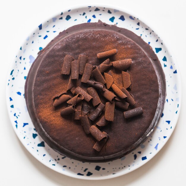 An elevated view of brown cake with chocolate shavings on white plate over the white backdrop