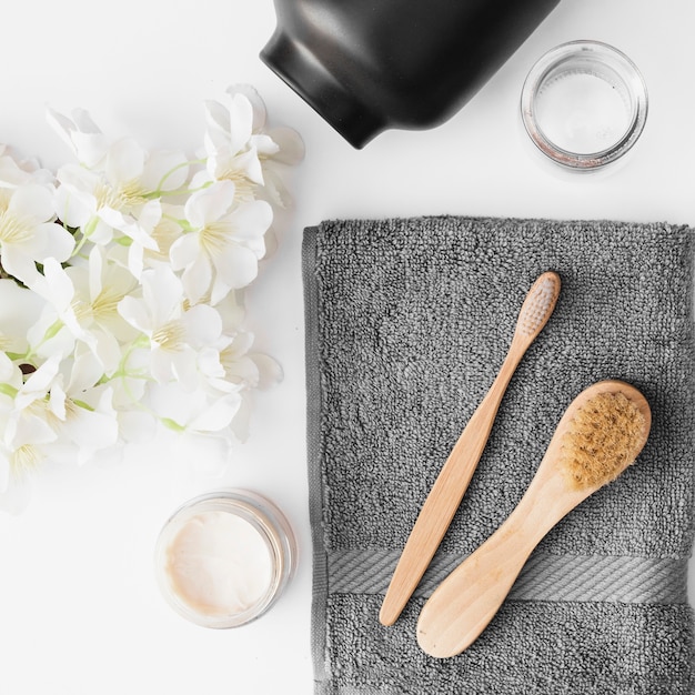 Elevated view of brush; towel; moisturizing cream; flowers and container on black backdrop