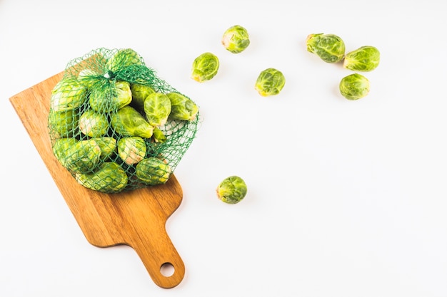 Elevated view of brussels sprouts in net on wooden chopping board