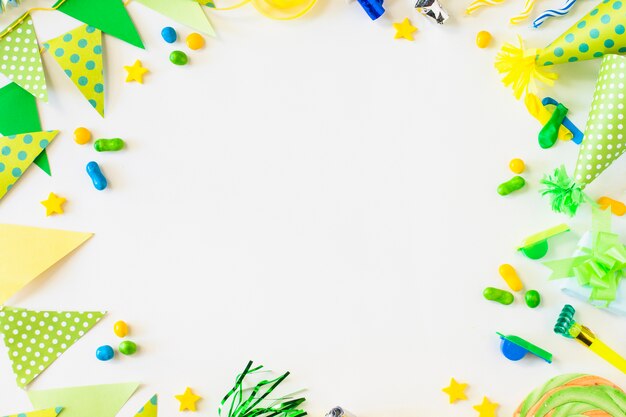 Elevated view of bunting; candies; party horn blower; whistle and hat on white surface