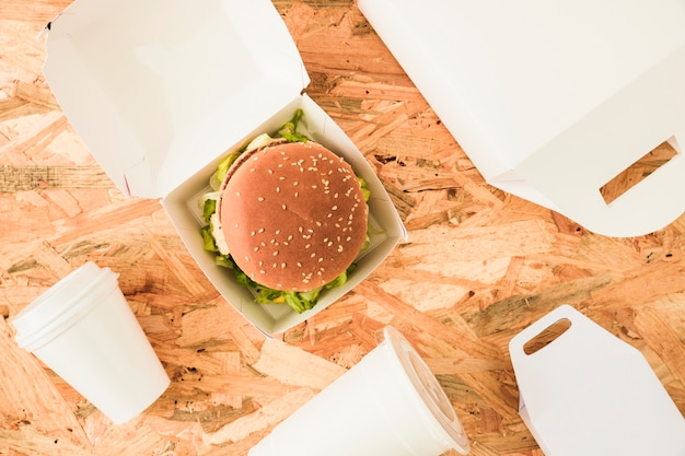 Elevated view of burger with disposal cups and packages on wooden background