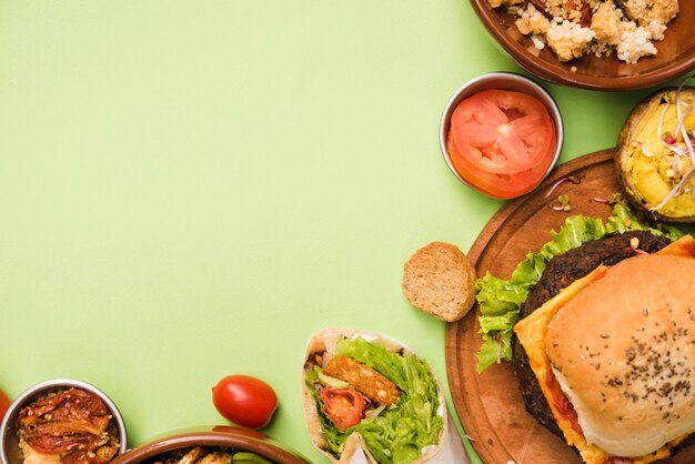 An elevated view of burrito wrap; salad and hamburger on green background