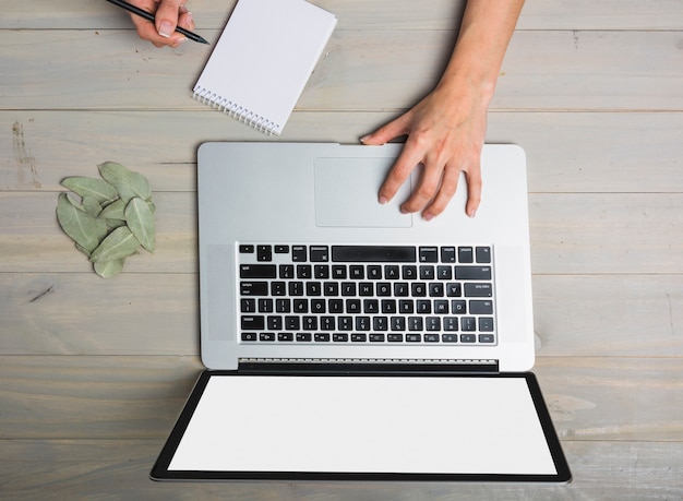 Elevated view of businessperson using laptop while writing on notepad