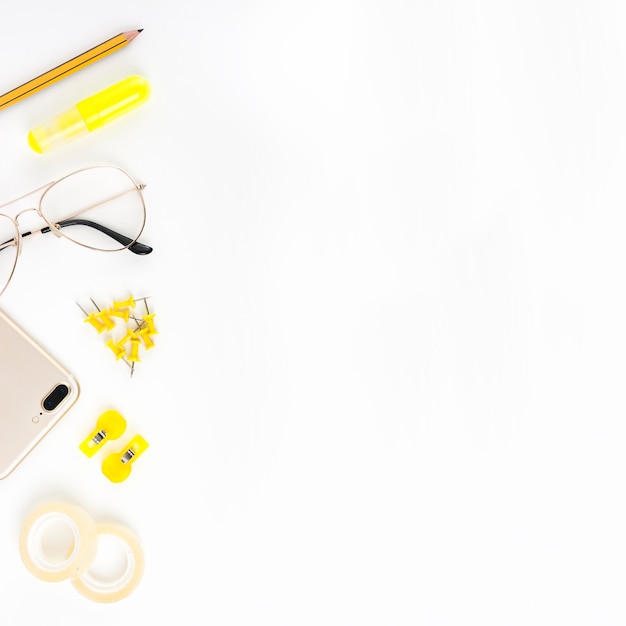 Elevated view of cellphone; spectacles and stationeries on white background