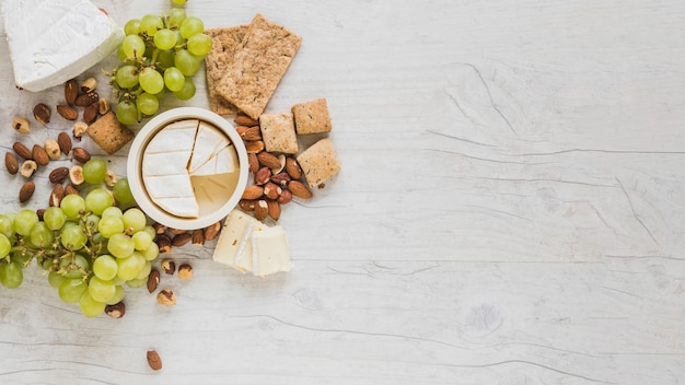 An elevated view of cheese cubes, grapes, dried fruits and crackers on grey wooden desk